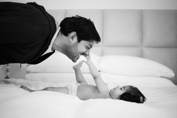 A father and baby play on a bed.