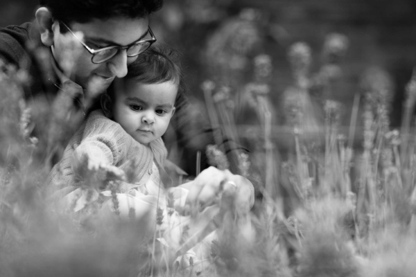 A father and their baby sit in a field during a London baby shoot.