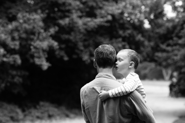 A father and child walk through trees.