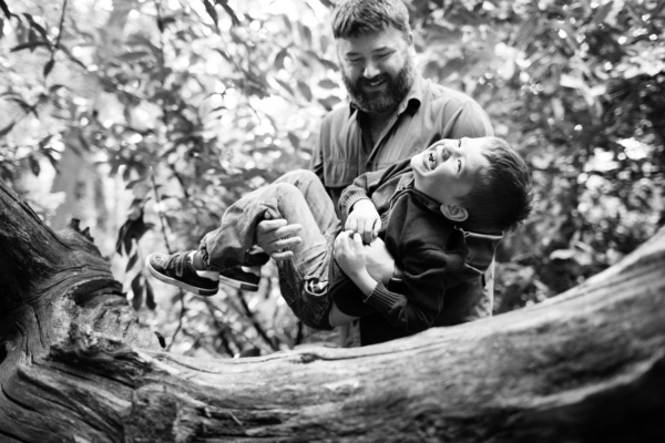 Father cradles his giggling son in the woods.