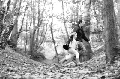 A father and daughter run through a woodland in the autumn.