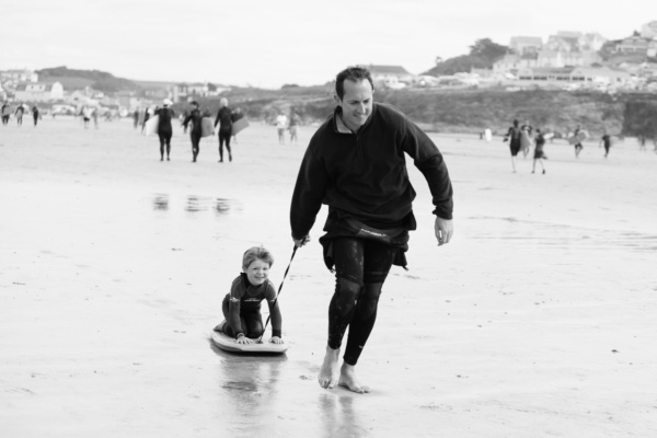 Father drags son along beach on his boogie board.