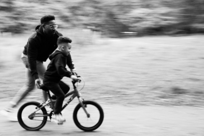 A father helps his child to ride his bike.