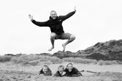 Father jumps over family on sandy beach.