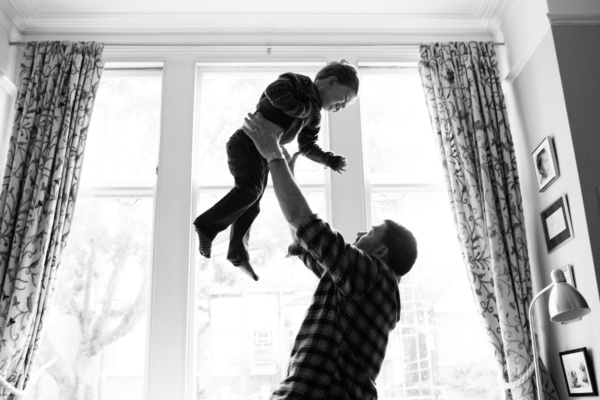 A father lifts his son in front of a window.