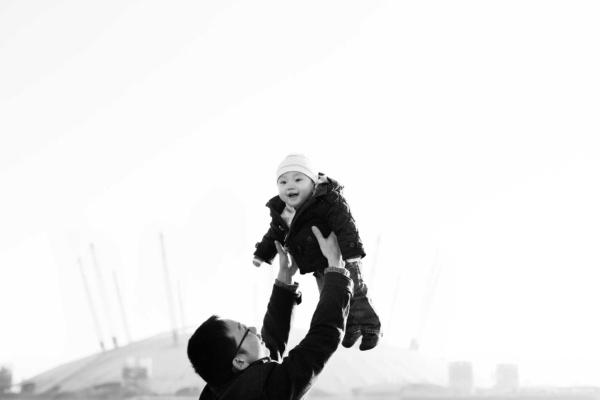 A father holds up his baby with Greenwich in the background, during their London family photo shoot.