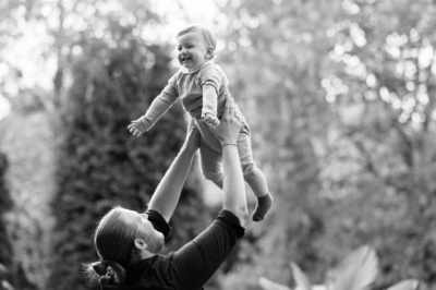 Father lifts up a giggling baby against a background of trees.