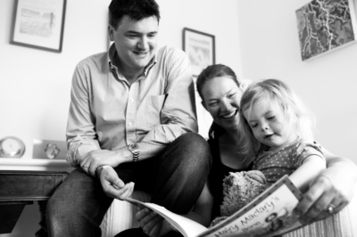 A father, mother and daughter read a book together.