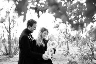 A new father and mother hold their newborn baby outdoors.