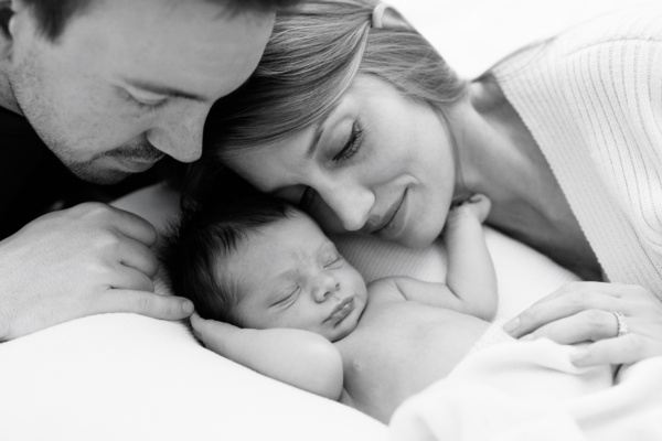 A father and mother snuggle their sleeping newborn baby.