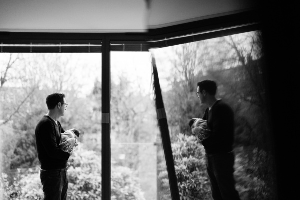 A father nurses his newborn while looking out of the window.