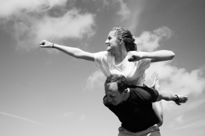 A father piggybacks his daughter against a cloudy sky.