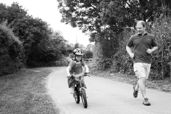 A girl rides her bike while her father runs alongside.