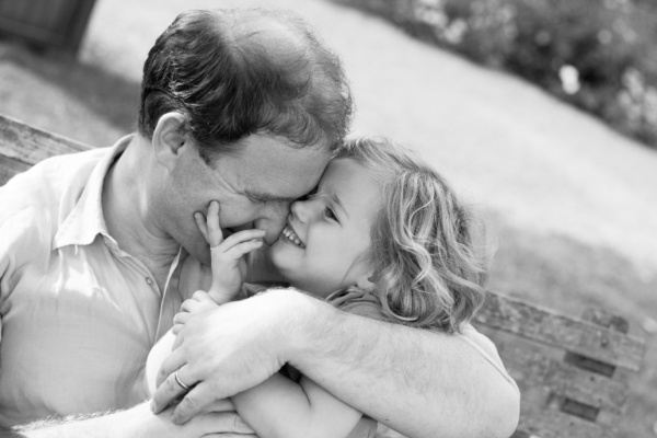 A father snuggles his daughter while sitting on a garden bench.