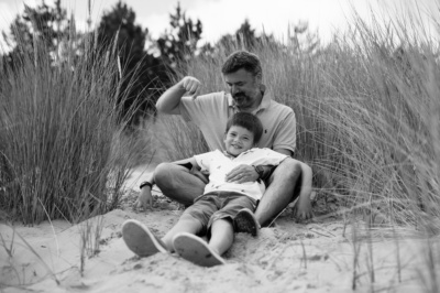 A father and son hug amongst sea grass on sand dunes.