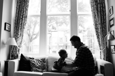 A father and his son play on a sofa together.