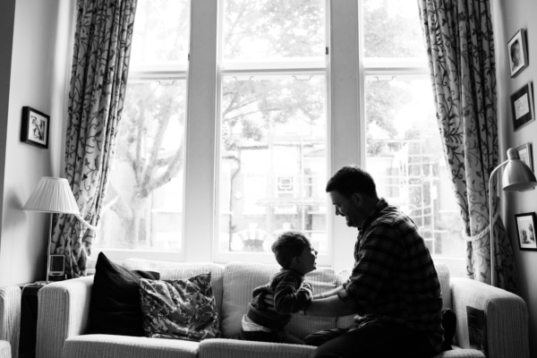 A father and his son play on a sofa together.