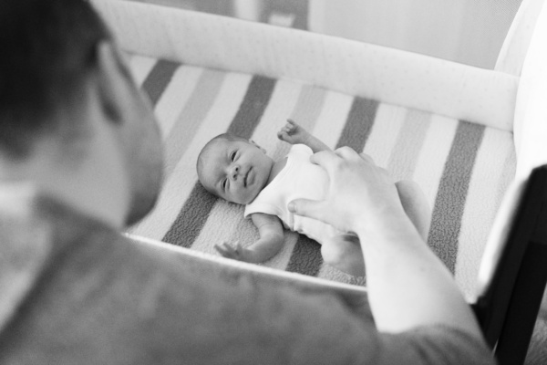 A father touches his newborn laying in a crib.