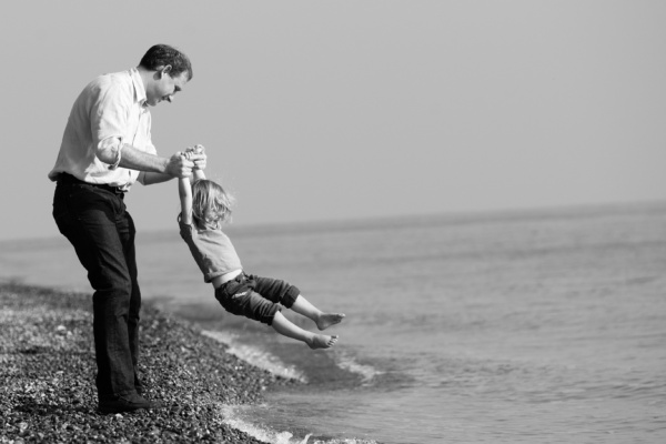 Father swings daughter into waves on a pebble beach.