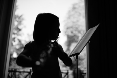 A flute playing teenager in silhouetted in a window.