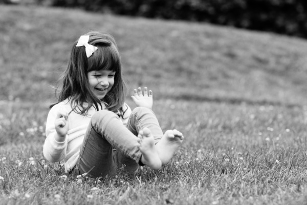 A barefoot girl in jeans giggles on grass.