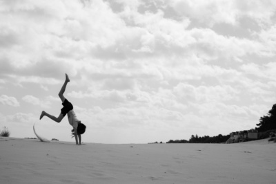 A girl cartwheels on sand.