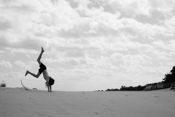 A girl cartwheels on sand.