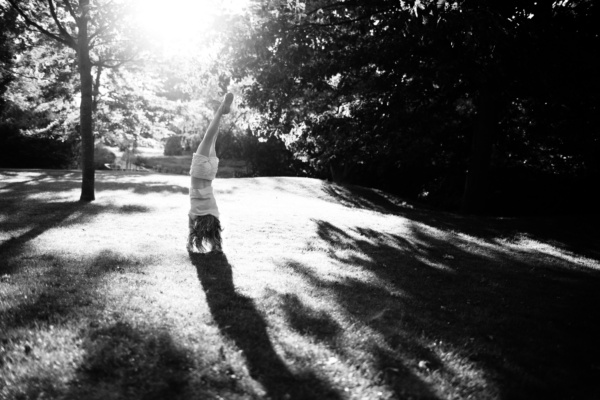 A girl does a handstand in a sunny garden.