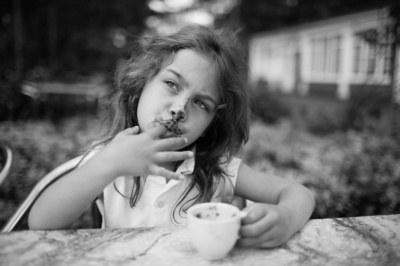 A girl eats dessert from a cup outdoors.