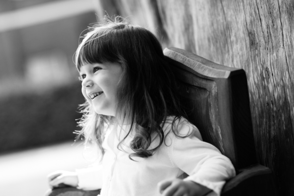 Girl on wooden seat giggles in the sunshine.