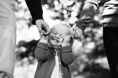 A girl holds onto her parents' fingers and smiles.