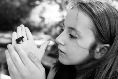 A girl holds a tiny frog in her hands.