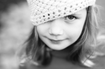 Girl in a crochet hat looks at the camera in a black and white portrait.