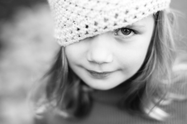 Girl in a crochet hat looks at the camera in a black and white portrait.