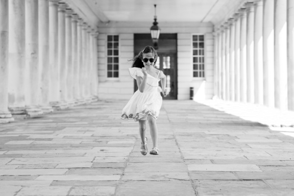 Girl in sunglasses runs between columns in Greenwich.