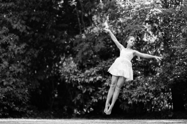 A girl jumps into the air in front of trees.