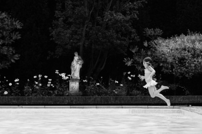 A girl jumps into a pool with a sculpture in the background.