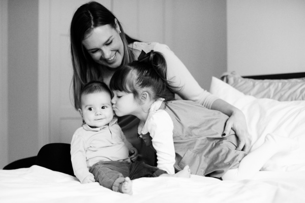 Girl kisses baby on the bed with their mother.