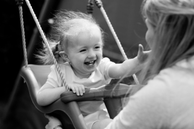 Girl laughs on swing being pushed by her mother.