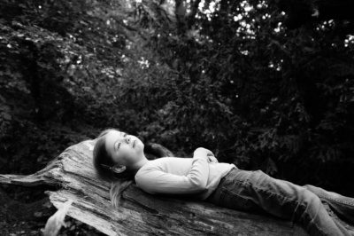 A girl lays on a log in the woods.