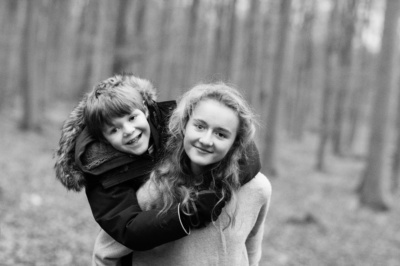 A girl piggybacks her brother through woodland.