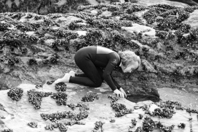 Girl in wetsuit looks in rock pools.