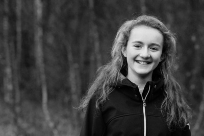 A girl smiles at the camera, against a backdrop of trees.