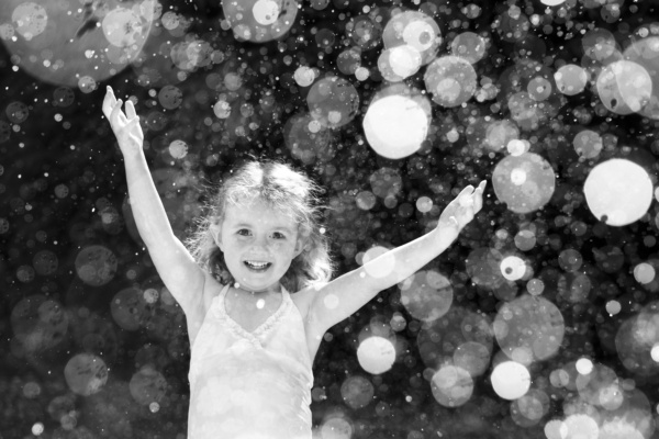 A girl smiles through water droplets.