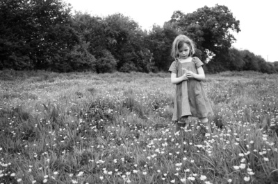 Girl stands in field of flowers, holding a flower.