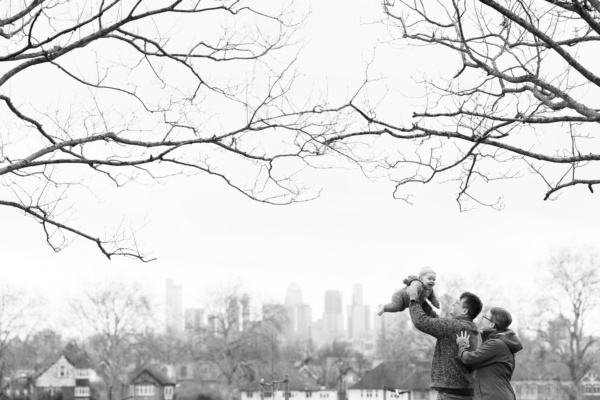 Parents and their toddler framed by trees, with London in the background.