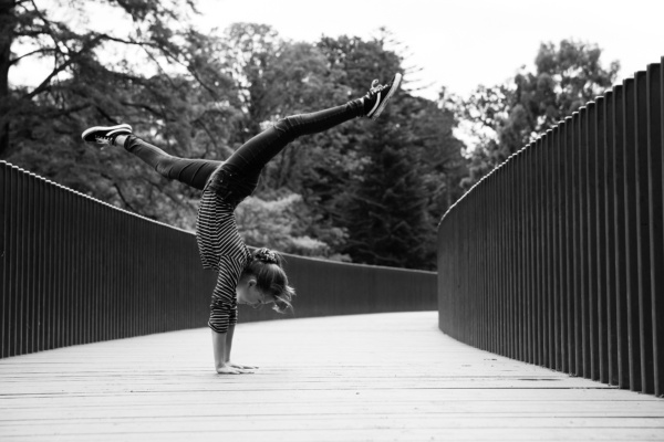 A gymnastic teen does a handstand on a wooden path.