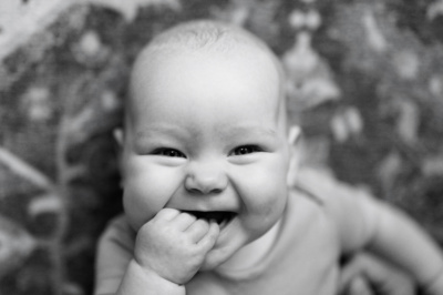 A laughing baby puts their first in their mouth.