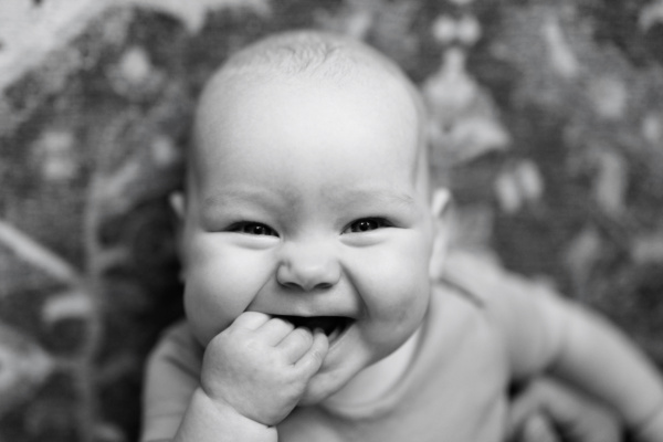 A laughing baby puts their first in their mouth.