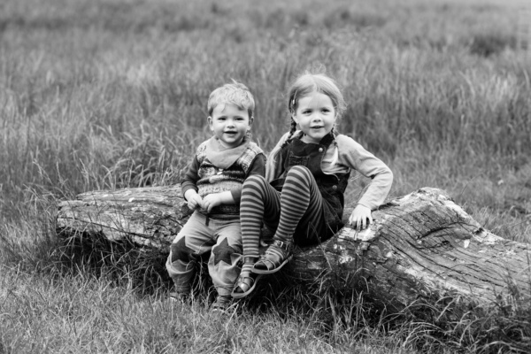 London children sit on a log together in the middle of a grassy field.